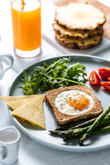 Sunny side up egg in a toast served with cheese, asparagus, rocket and tomatoes on a rustic white background
