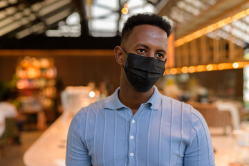 Fototapeta na wymiar African businessman wearing face mask in coffee shop restaurant while thinking
