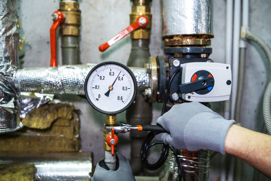 Repair of equipment in an industrial boiler room.  A plumber with a wrench and wearing work gloves corrects problems at the connection point of the pressure gauge