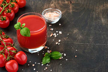 Glass of fresh tomato juice, salt, basil and tomatoes on  wooden stand  on old wooden background. With copy space.