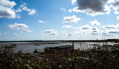 Empty estuary deserted in spring sun with abandoned boat on shore