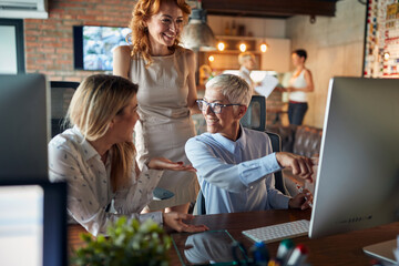 A senior business woman is showing a content on a computer screen to her female colleagues at the workplace. Business, office, job