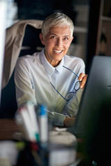 A cheerful senior business woman is posing for a photo while working at the workplace. Business,...