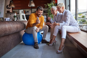 A young male businessman showing a smartphone content to his elderly female colleagues while they take a break at workplace. Business, office, job