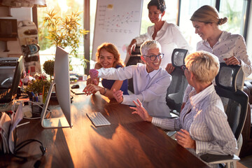 An elderly female boss is explaining a computer screen content to her female colleagues while they...