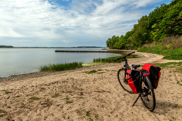 Fototapeta premium Fahrrad am strand, am see mit Sand und Wolken und Wald, Fahrradtour, Fahrradwanderung mit Fahrrad und Fahrradtaschen