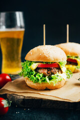close-up of a hamburger with meat on a grill tomato and greens on the background of a glass with beer on a black background
