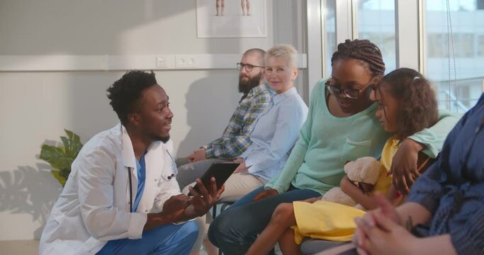 Afro-american male doctor talking to mother and kid in hospital waiting room