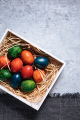 Easter eggs in box with golden hay on a rustic plain grey background
