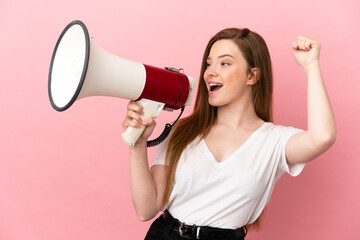 Teenager girl over isolated pink background shouting through a megaphone to announce something in lateral position - obrazy, fototapety, plakaty