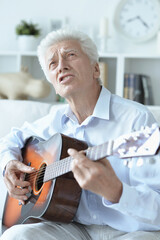 happy senior man with guitar  sitting on the sofa at home