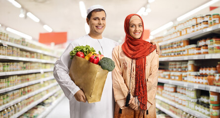 Young muslim couple in a supermarket holding a paper shopping bag with groceries