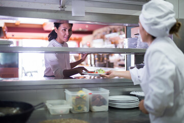 Fototapeta na wymiar smiling female waiter geting order from chef in restaurante