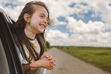 Little kid dreaming from an open car window while travelling. Summer trip with family