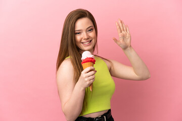 Teenager girl with a cornet ice cream over isolated pink background saluting with hand with happy expression