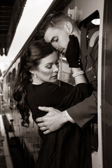 Vintage couple, man in uniform, woman in red dress, holding hands goodbye at train station as train departs