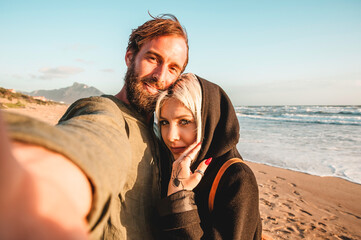 Traveling couple in love taking selfie in a deserted beach at sunset - Woman with magnetic gaze and...