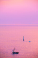 Tourist yachts boat in Aegean sea near Santorini island with tourists watching sunset viewpoint. Santorini, Greece
