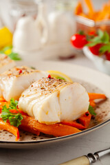Fried pieces of cod loin, served with sweet potato fries. Light stone background.