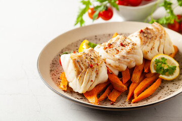 Fried pieces of cod loin, served with sweet potato fries. Light stone background.