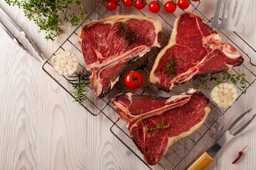 Raw t bone steak, with herbs. Grill accessories. Ready for grilling. Wooden bright background.