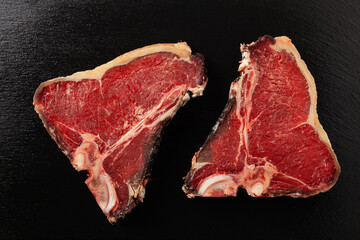 Raw t bone steak, with herbs. Black stone background. View from above.