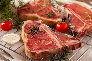 Raw t bone steak, with herbs. Grill accessories. Ready for grilling. Wooden bright background.