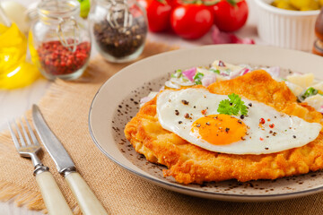 Viennese pork schnitzel with a fried egg. Served on potato salad. Natural wooden planks in the background.