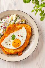 Viennese pork schnitzel with a fried egg. Served on potato salad. Natural wooden planks in the background.