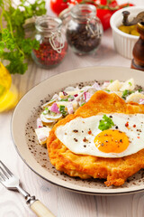 Viennese pork schnitzel with a fried egg. Served on potato salad. Natural wooden planks in the background.