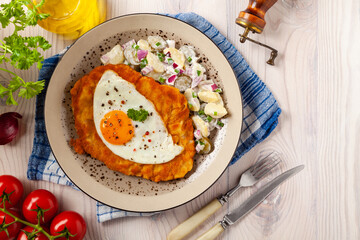Viennese pork schnitzel with a fried egg. Served on potato salad. Natural wooden planks in the background.