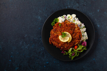 Classic, traditional Viennese sirloin schnitzel. Served on potato salad. Breaded. Dark background.