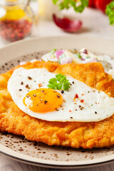 Viennese pork schnitzel with a fried egg. Served on potato salad. Natural wooden planks in the...