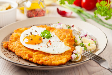 Viennese pork schnitzel with a fried egg. Served on potato salad. Natural wooden planks in the...