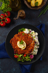 Classic, traditional Viennese sirloin schnitzel. Served on potato salad. Breaded. Dark background.