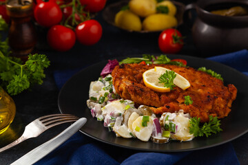 Classic, traditional Viennese sirloin schnitzel. Served on potato salad. Breaded. Dark background.