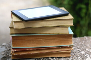 Stack of vintage hardcover books and e-reader on top. Selective focus.