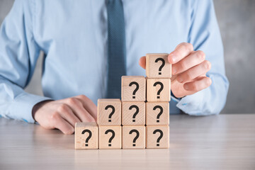 Businessman hold and put wooden cube block shape with question marks on grey table. Space for text.concept for confusion, question or solution