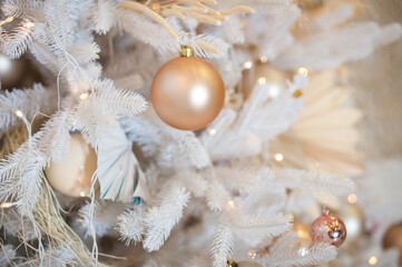 White Christmas decoration with balls on fir branches with blurred background. White Christmas tree with beige Christmas balls and lights.