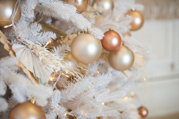 Fototapeta na wymiar White Christmas decoration with balls on fir branches with blurred background. White Christmas tree with beige Christmas balls and lights.