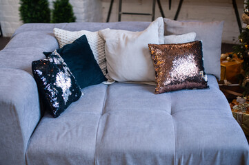 Several shiny and beige decorative pillows on a cozy gray sofa, interior.