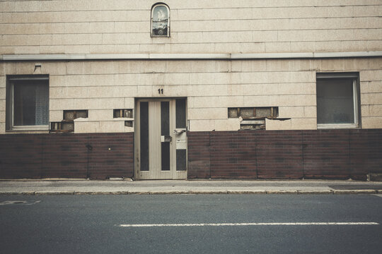 Facade Of A Beige And Brown Old Building With Defective Walls Near The Asphalt Road