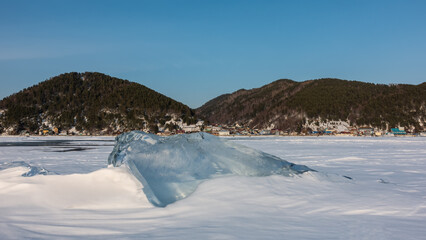 Transparent glittering ice floe in the middle of a frozen and snow-covered lake. Sun glare on the...