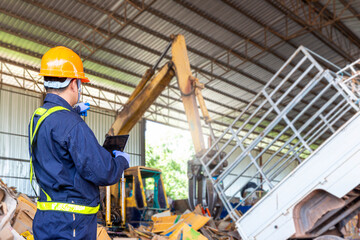 A worker holding a tablet in a recycling plant stands in the process of recycling paper with cranes and loaders.