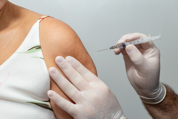 Mãos de médico ou enfermeiro aplicando vacina no braço de paciente.