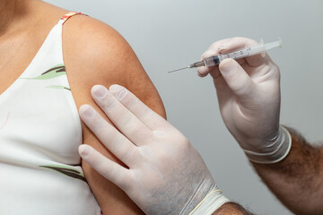 Mãos de médico ou enfermeiro aplicando vacina no braço de paciente.