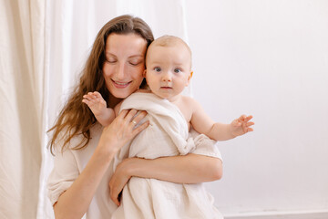 Mom hugs baby on a white background. Eco parenting concept. White clothes and a diaper  natural fabrics linen cotton muslin.  Mother's love. Hugs, smiles, happiness. Mother and child togetherness