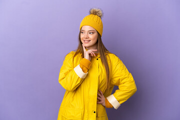 Teenager girl wearing a rainproof coat over isolated purple background thinking an idea while looking up