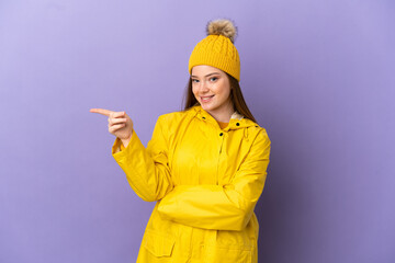Teenager girl wearing a rainproof coat over isolated purple background pointing finger to the side