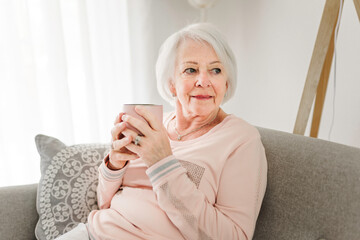 portrait of elderly woman sit on the sofa at home with coffee or tee